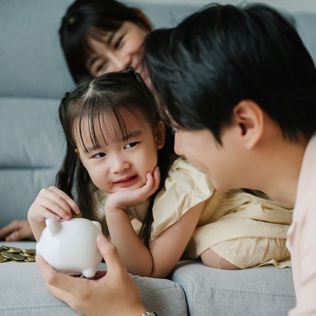Young girl holding a piggy bank while smiling at her father, symbolizing financial planning and securing a bright future for the next generation.
